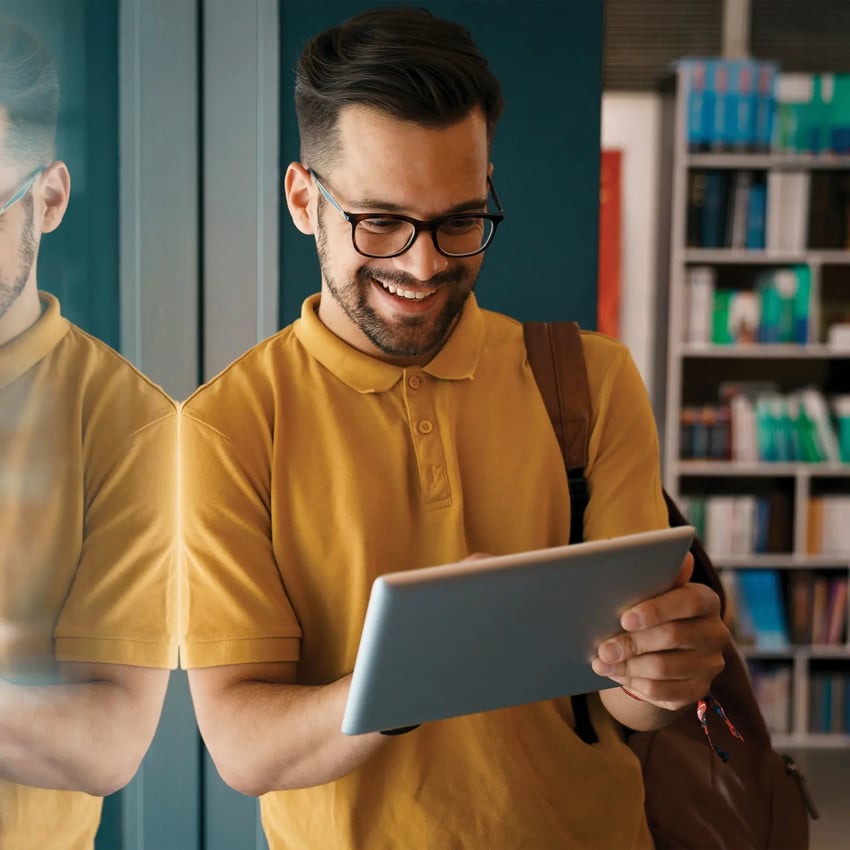 Young man wearing glasses standing, holding an ipad smiling.