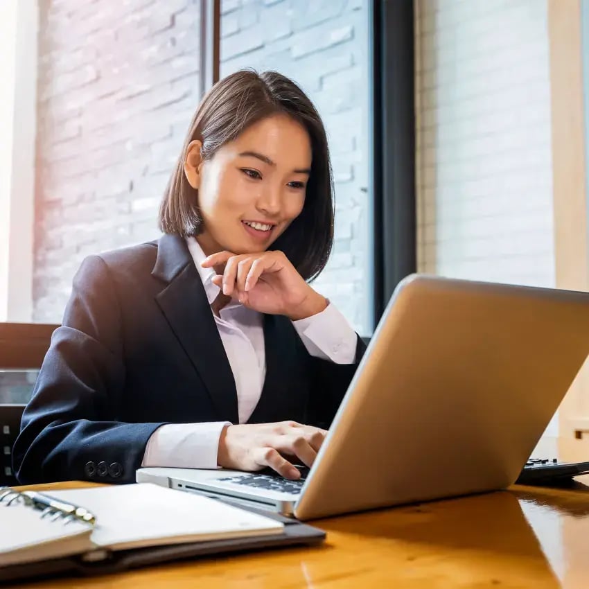 A young woman looking at her laptop and smiling.