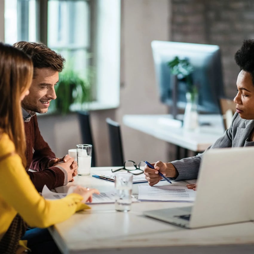 Three colleagues engaged in a focused discussion about their CeMAP, around a table in a modern office setting.