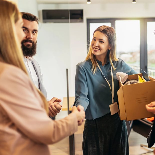 A young woman shaking hands and holding a box.