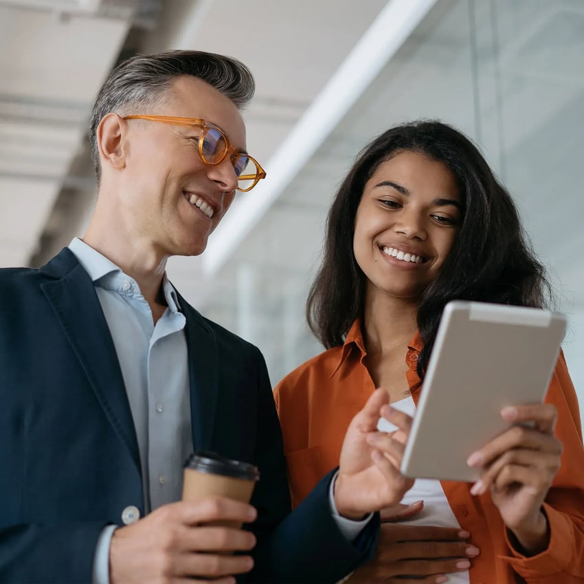 A man and a woman standing and smiling at an ipad.