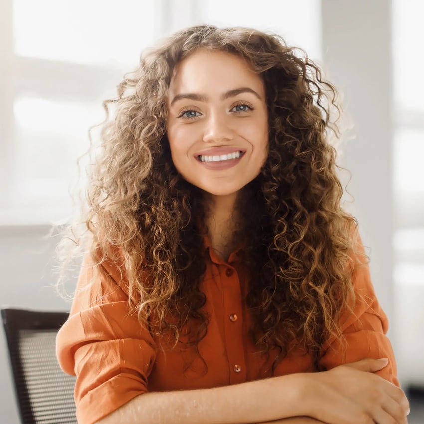 Young woman wearing an orange buttoned shirt and smiling.