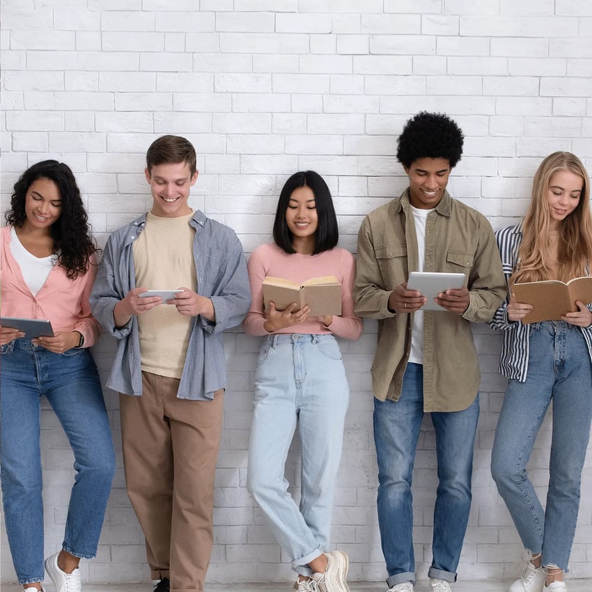 A group of teenagers standing and looking at books or ipads.