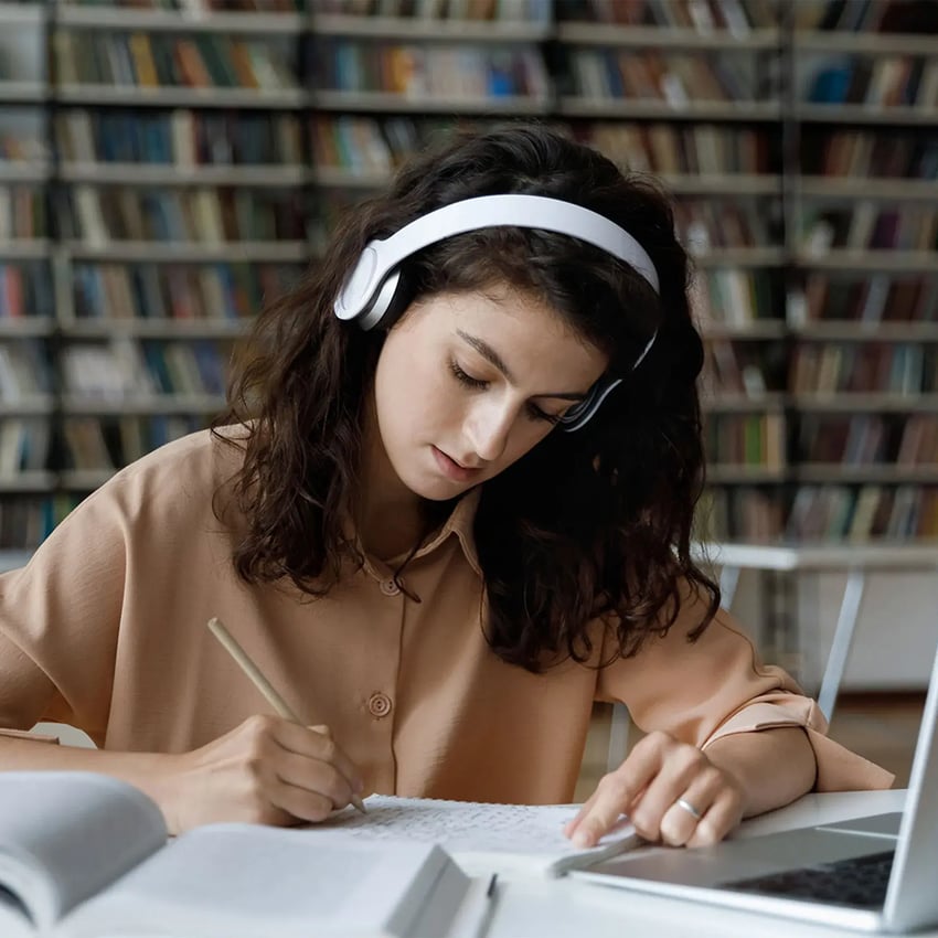 A young girl wearing headphones and writing in her notebook.