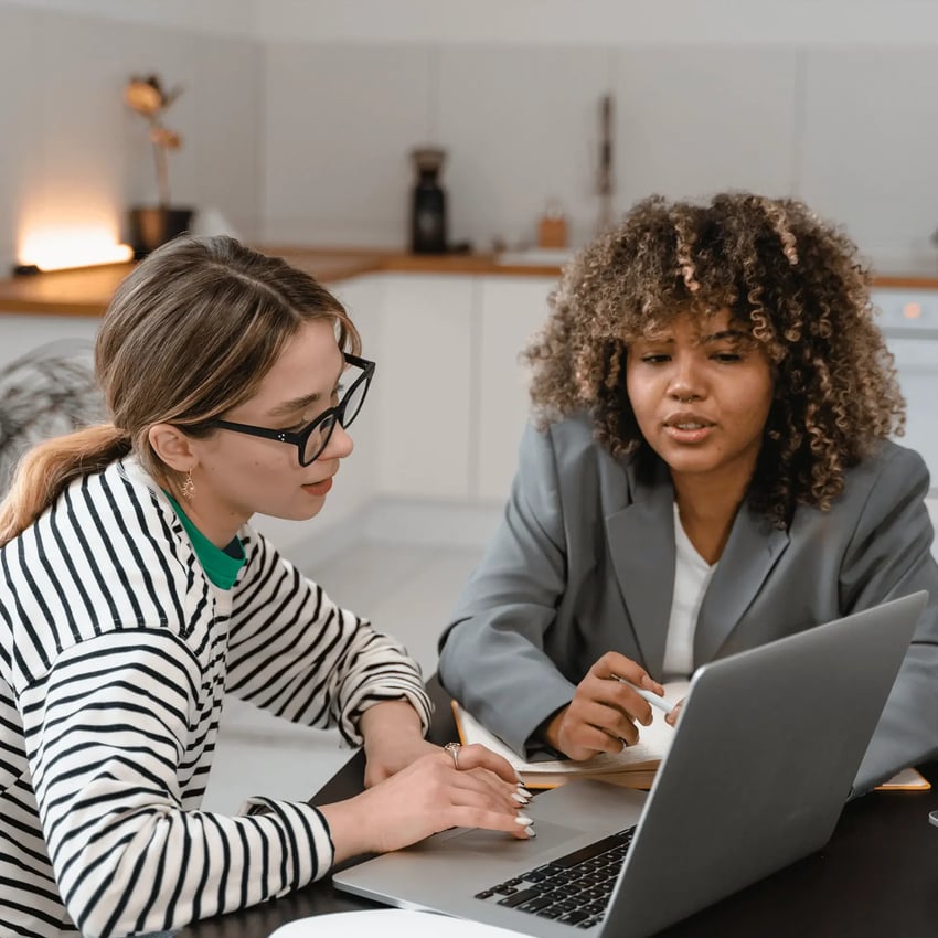 Two young women intently focused on a laptop screen, working on payments certification.