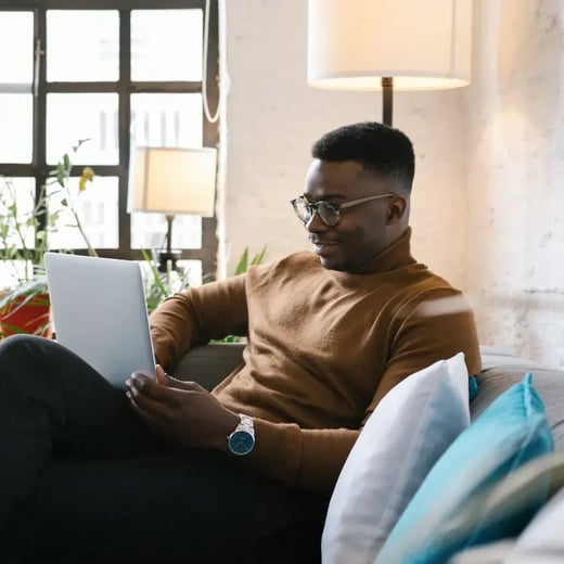 Man in brown jumper studies an online degree at laptop from home